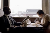 A driver sits in a booth eating breakfast with an African-American classical pianist