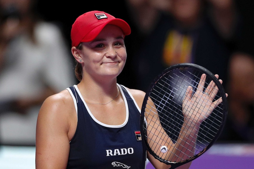 Ash Barty smiles and claps on her racquet while looking at the crowd.