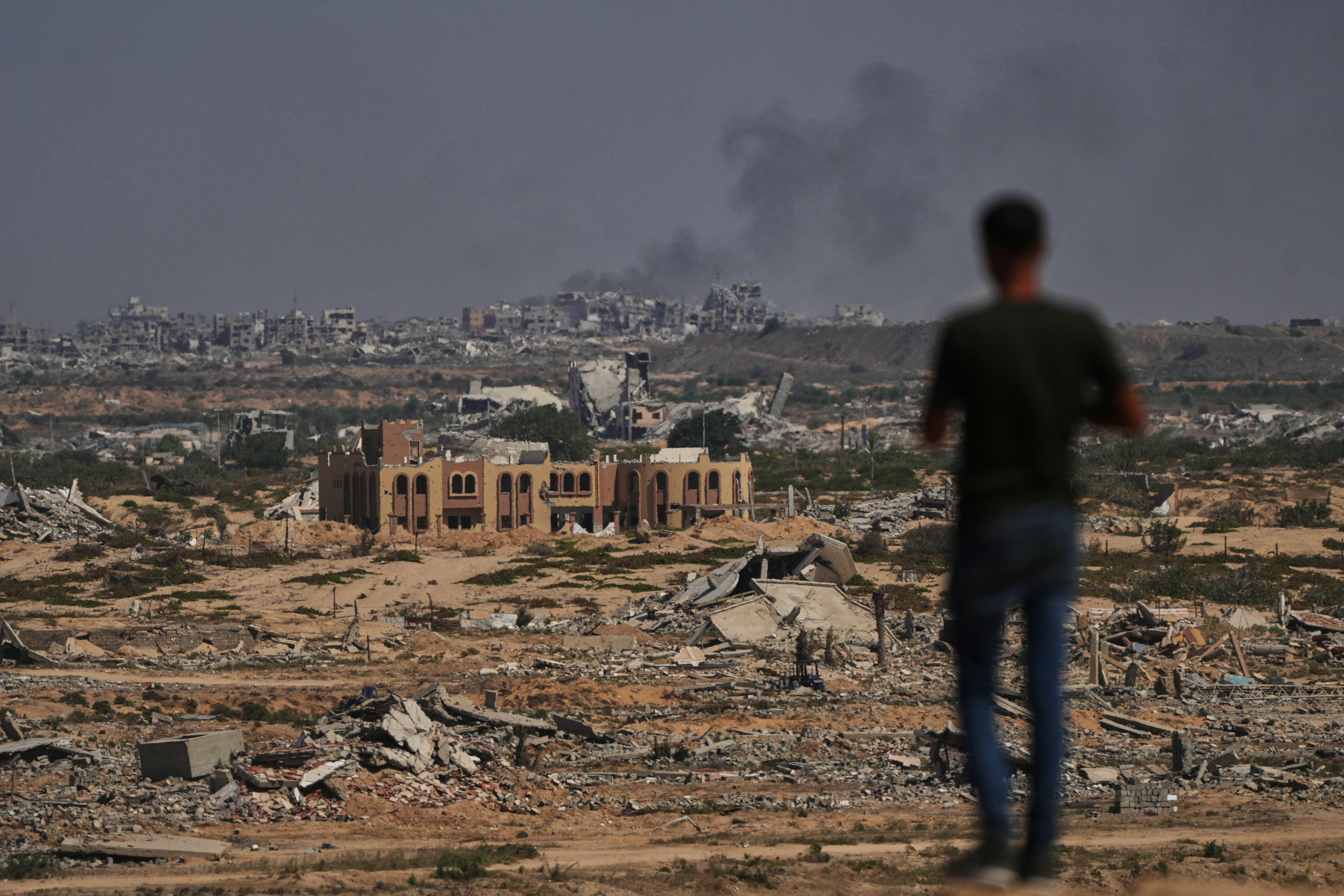 A man looks out at a flattened Gaza City that’s been turned to rubble and is smoking