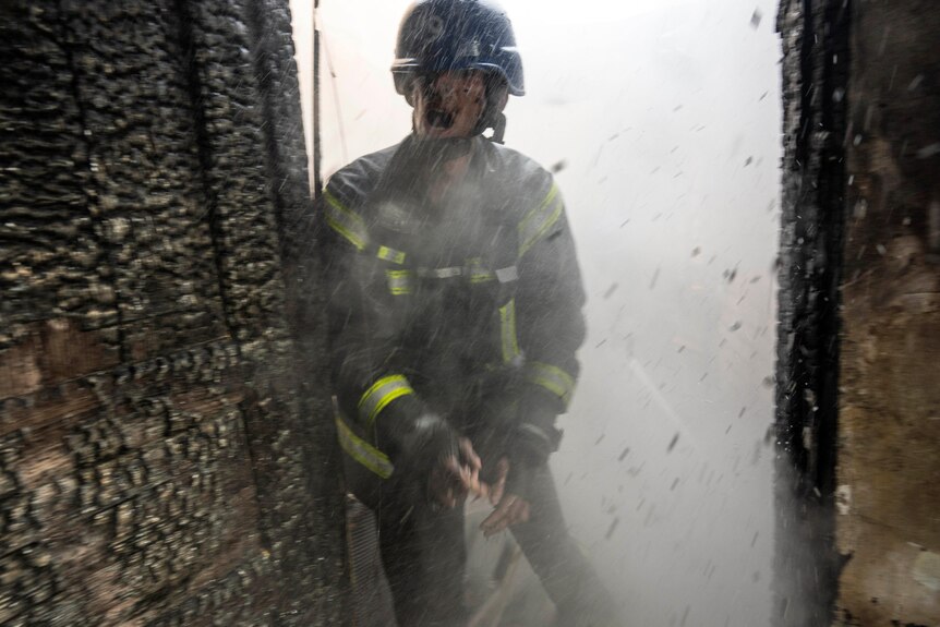 A person in a firefighting uniform shouts through a doorway as debris falls around them