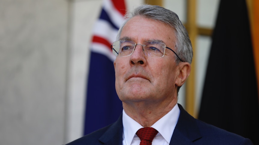 Dreyfus looks pensive with an Australian flag visible behind him.