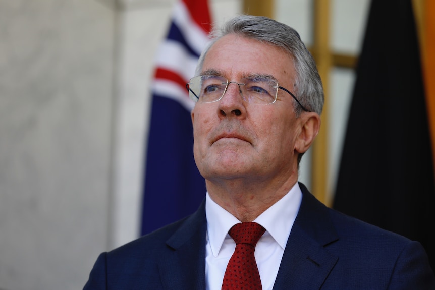 Dreyfus looks pensive with an Australian flag visible behind him.