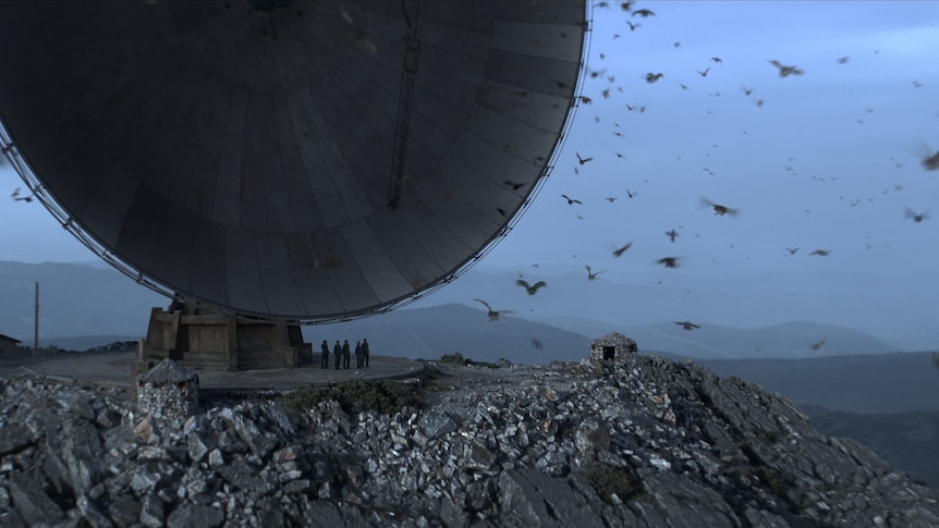 A satelite dish surrounded by birds on a hilly clifside. 