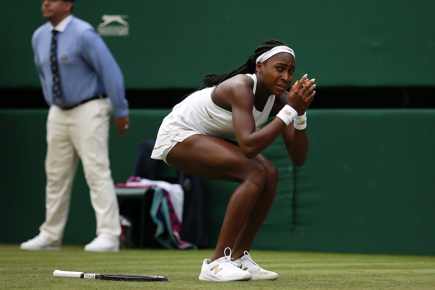 Coco Gauff bends down and hides her face in her hands with her racquet by her side