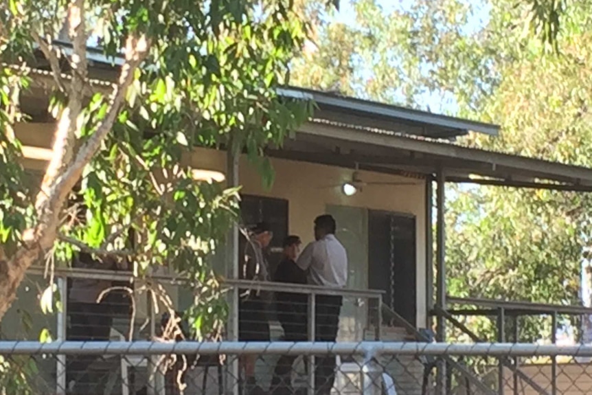 Three officials stand on the verandah of a cabin.