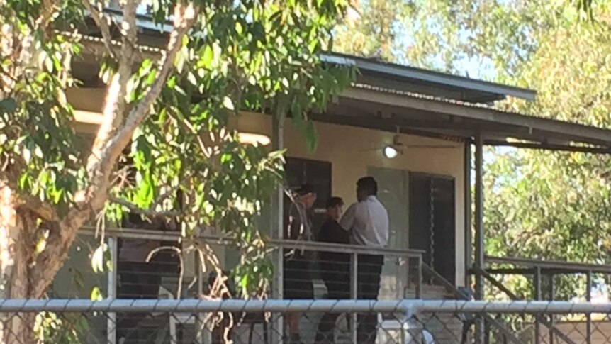 Three officials stand on the verandah of a cabin.
