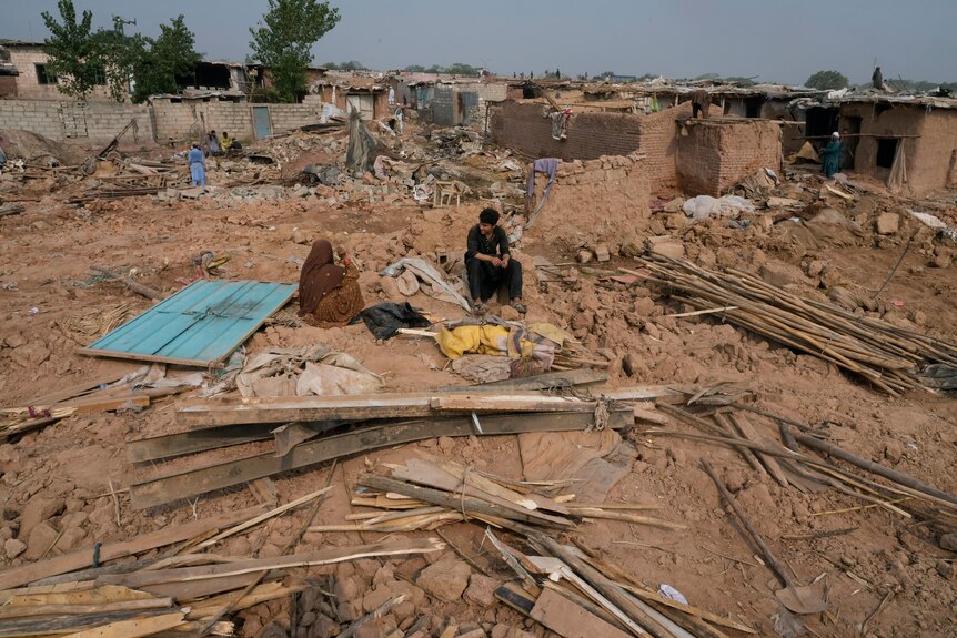 An Afghan family rests near rubble as others retrieve useful stuff from their demolished mud homes.