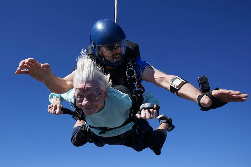 An elderley woman sky diving with a man behind her. 
