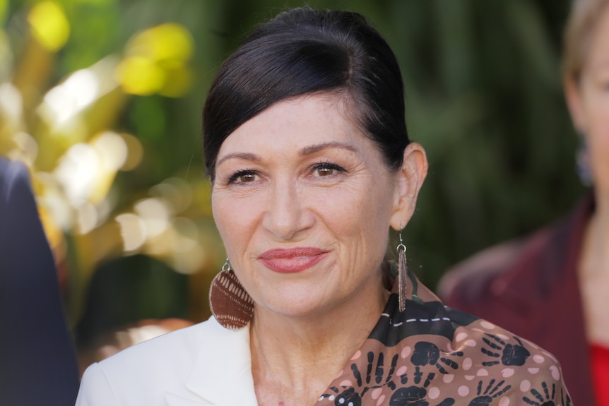 A close-up of Leeanne Enoch  smiling with trees behind her.