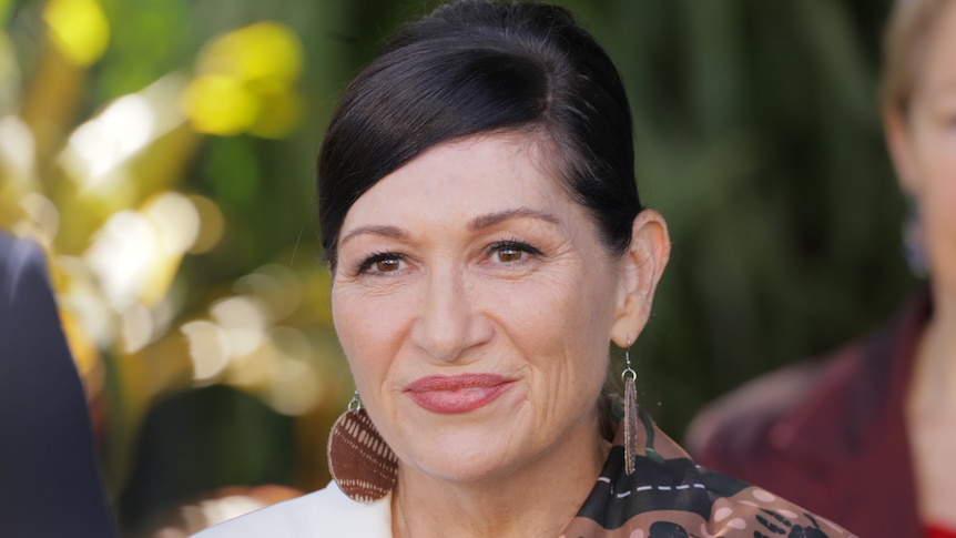 A close-up of Leeanne Enoch  smiling with trees behind her