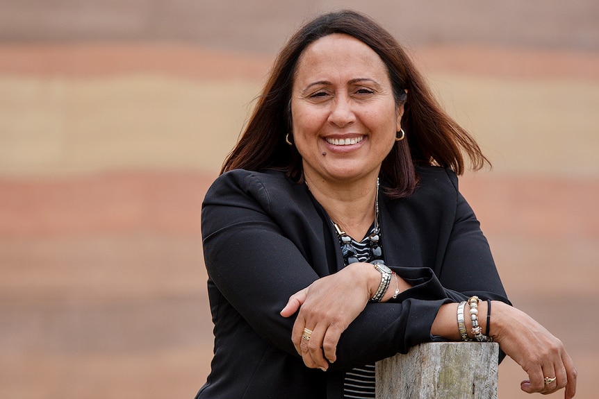 A smiling woman leans on a wooden post