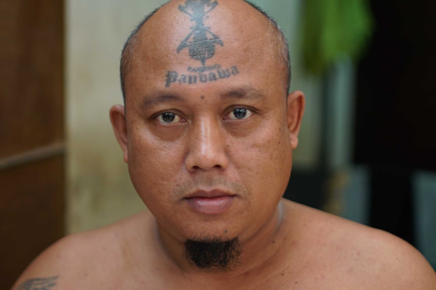 A man with a forehead tattoo that says "Panbawa" looks into the camera, taken inside Kerobokan prison.