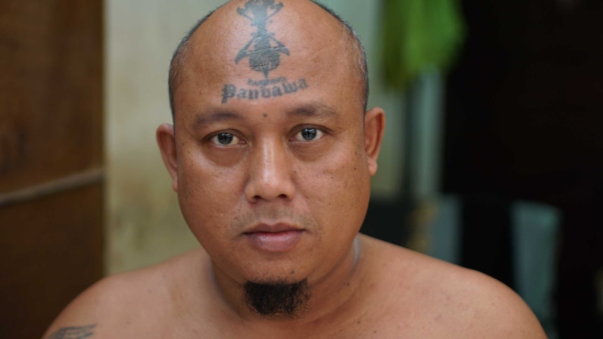 A man with a forehead tattoo that says "Panbawa" looks into the camera, taken inside Kerobokan prison.