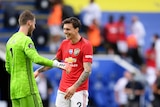 Premier League goalkeeper and one of his team's defenders grin at each other after winning a match.