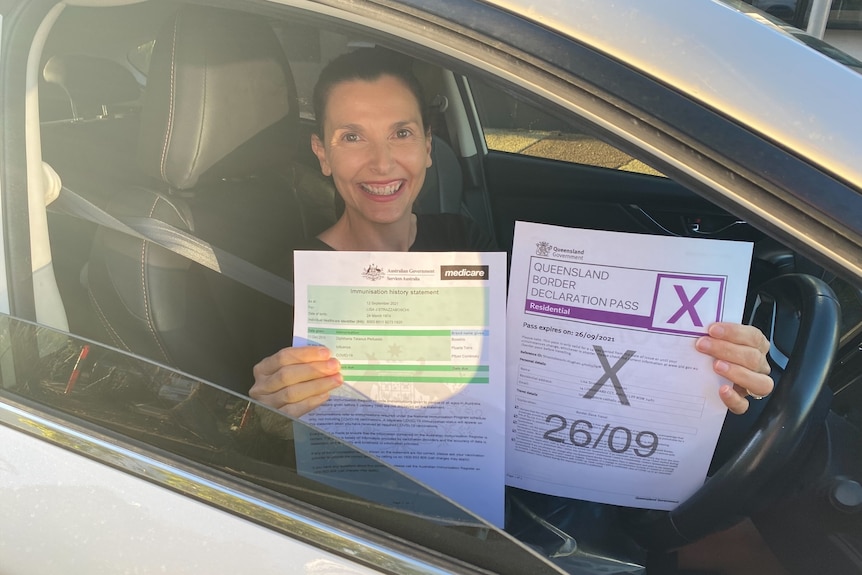 A woman smiling with paperwork, sitting in her car.