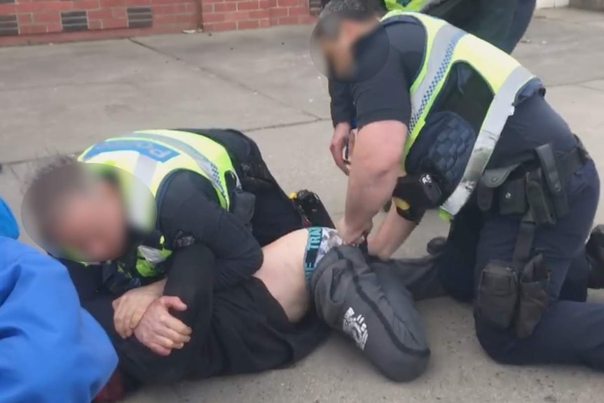 A police officer holds a man down while another officer holds his legs.