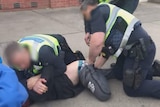 A police officer holds a man down while another officer holds his legs.