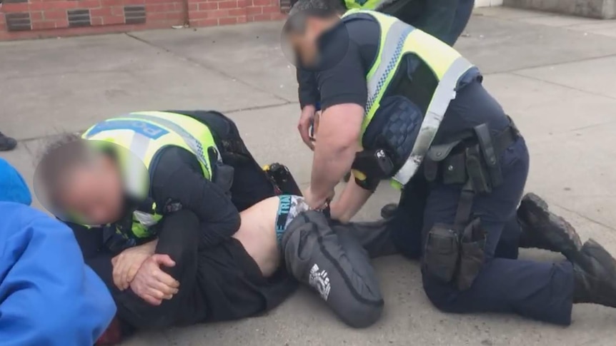 A police officer holds a man down while another officer holds his legs.