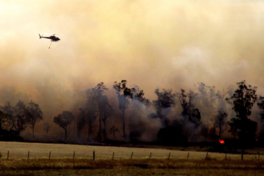 A water-bombing helicopter flies over a bushfire.