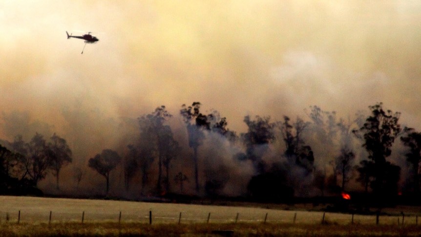 A water-bombing helicopter flies over a bushfire.