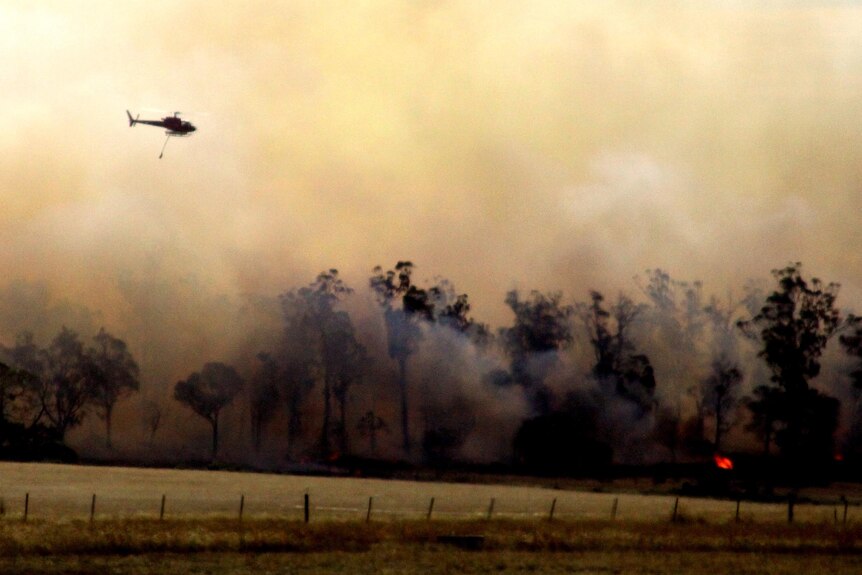 A water-bombing helicopter flies over a bushfire.