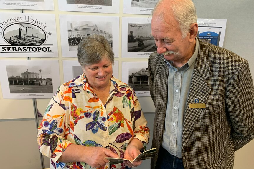 An older woman and man look at a booklet, smiling.