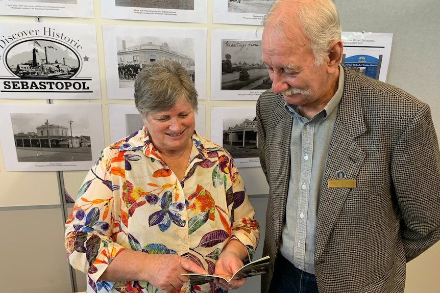 An older woman and man look at a booklet, smiling.