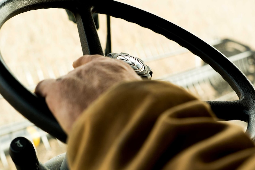 A man's left hand rests on the steering wheel of a soybean harvester.
