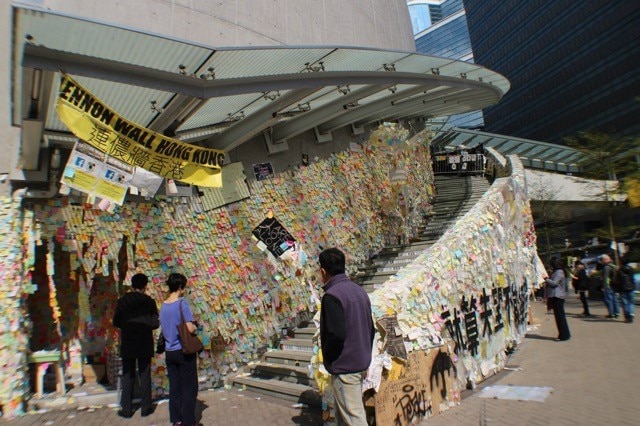 People look at walls covered in sticky notes of different colours.