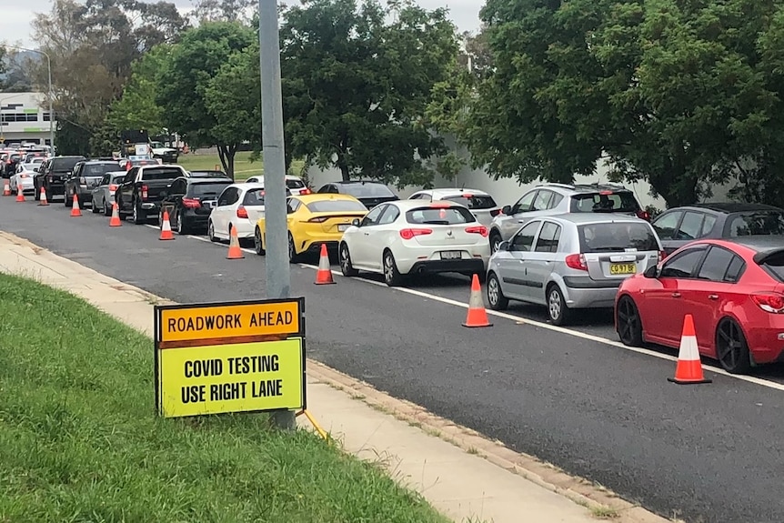 Cars queue along a road near a sign reading 'COVID testing use right lane'.