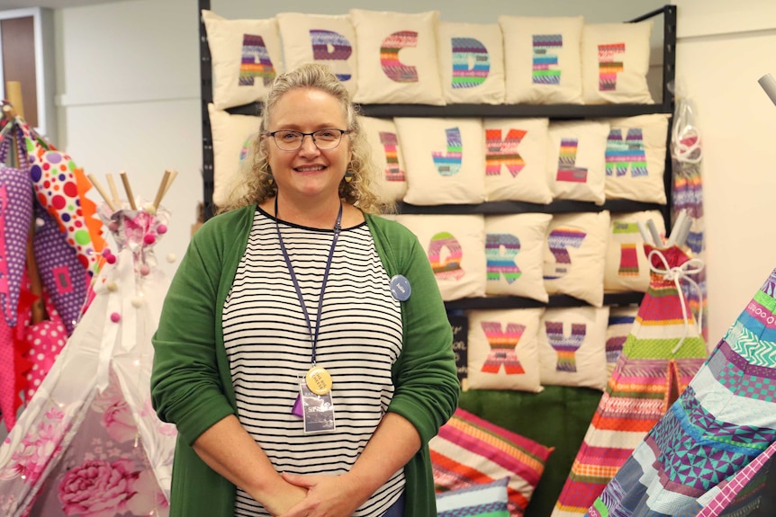 A woman stands in front of brightly coloured pillows and children's play equipment.