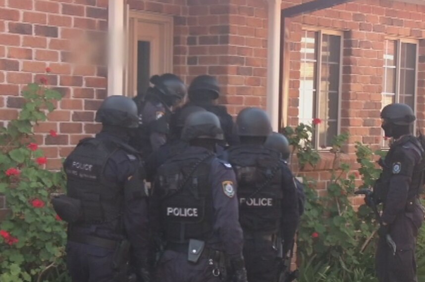 Police gather at the front door of a Padstow home during early morning raid.