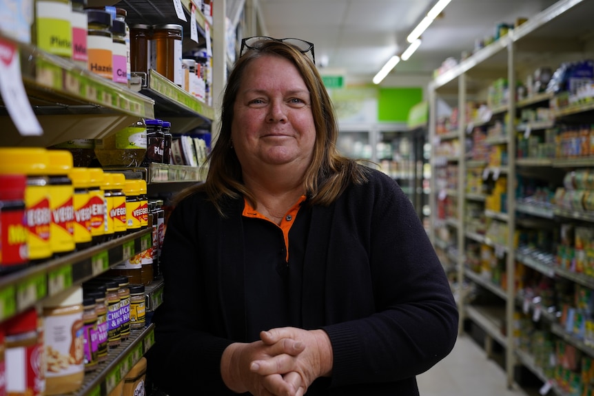 A woman stands in an aisle of a grocery store and smiles at the camera