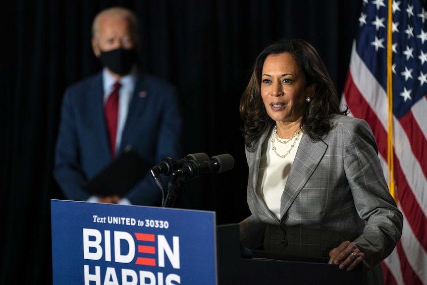 Kamala Harris speaks at a microphone with Joe Biden watching on in the background