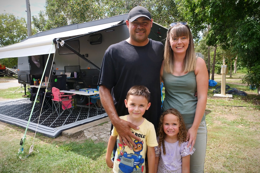 A mother and father stand before two children - a boy and a girl. Behind the family is their campsite.