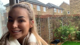 Grace Calvert smiles with a big winter scarf, she is in front of a window that looks out into a small yard at her home.