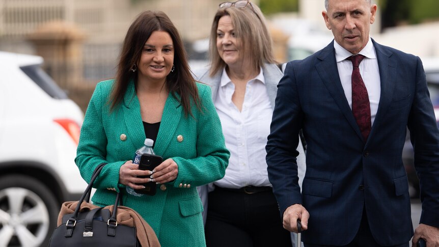 Jacqui Lambie smiles and speaks with a man and she walks down a path.