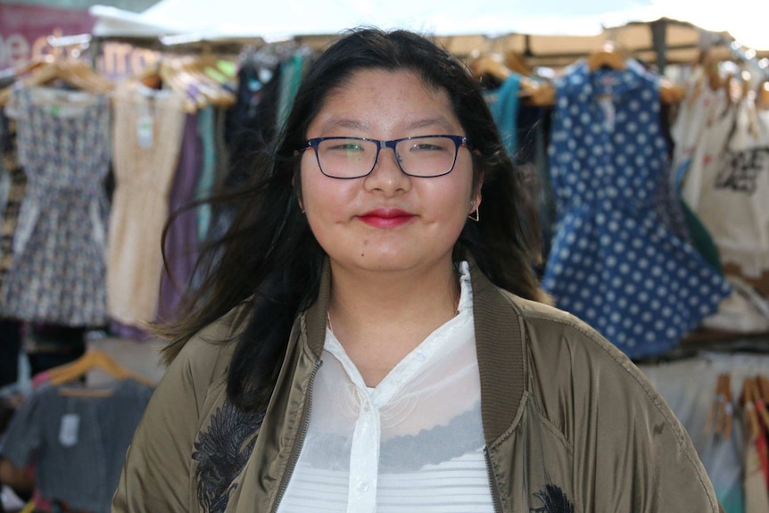 A teenage girl in front of clothes racks.