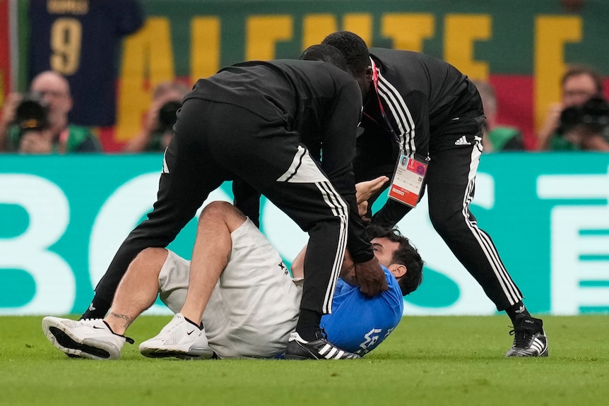 Two referees tackle a protester to the ground on a soccer field