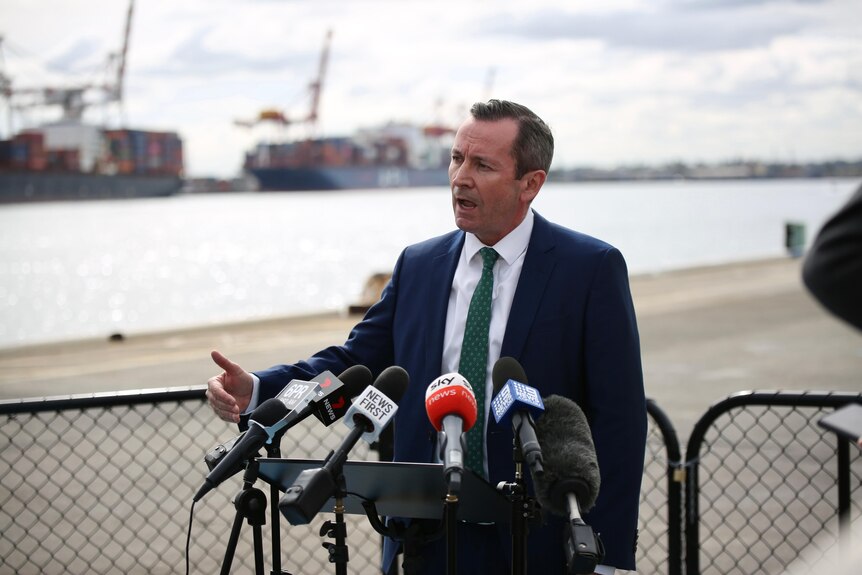 WA Premier Mark McGowan mid-speech in front of a row of media microphones.