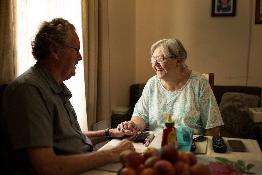 elderly man and woman holding hands and smiling near a sunlit window