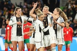 A German striker makes a phone call gesture with her hand as she receives congratulations for a goal.