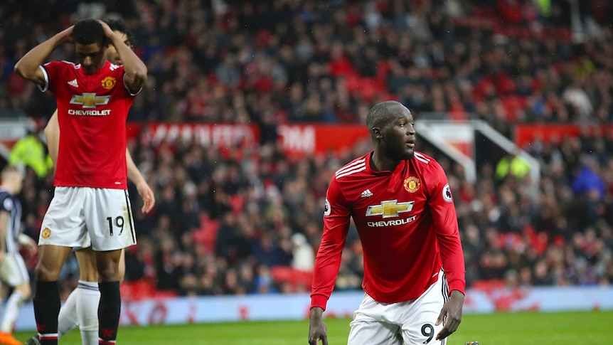 Manchester United player Marcus Rashford holds hands to head, Romelu Lukaku slumps to ground