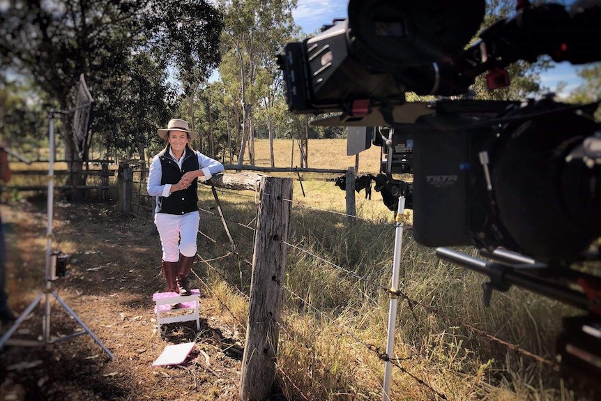 Pip Courtney stands in paddock with camera in foreground