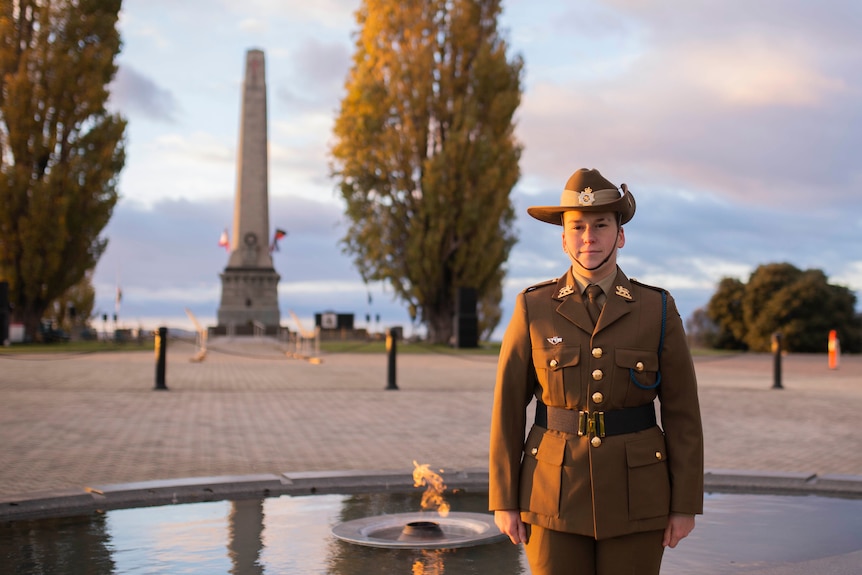 A young woman in uniform stands at a cenotaph