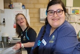 Two girls tidying school kitchen and smiling at camera