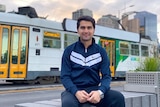 A young man smiling at the camera with a Melbourne tram in the background.