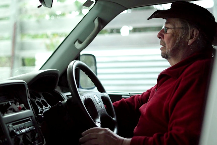 A man in a hat sits behind a car's steering wheel.