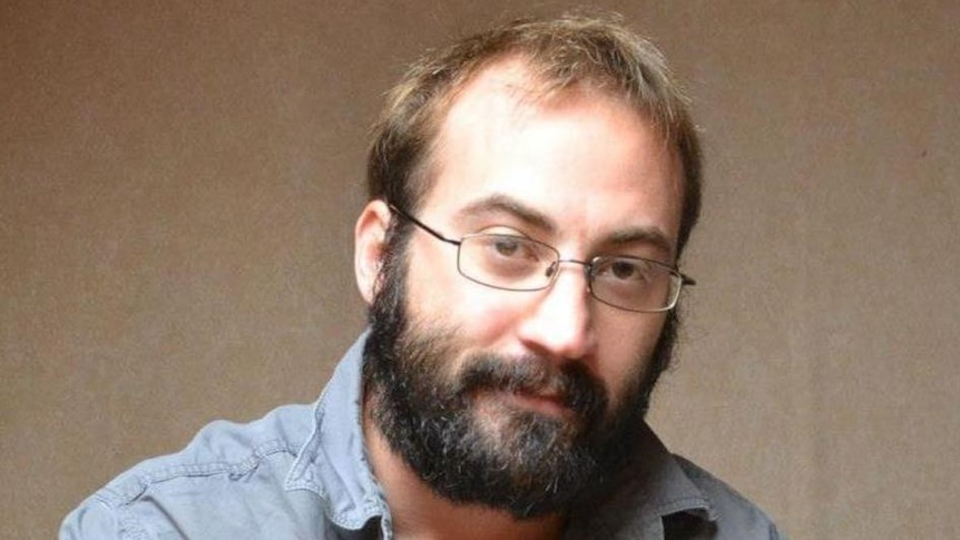 A balding man with glasses has a small smile towards the camera.