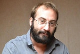 A balding man with glasses has a small smile towards the camera.